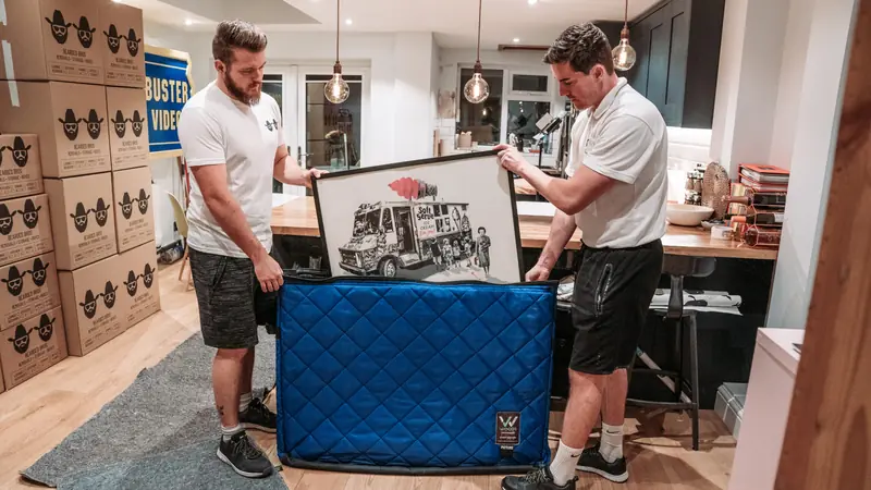 Two Bearded Bros crew members packing a framed picture into a protective picture case in a customer's kitchen