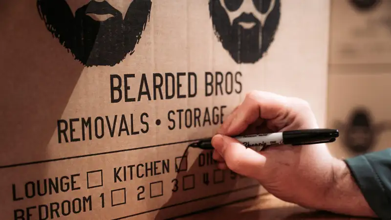 Hand ticking a room checkbox on a Bearded Bros branded moving box with a marker pen