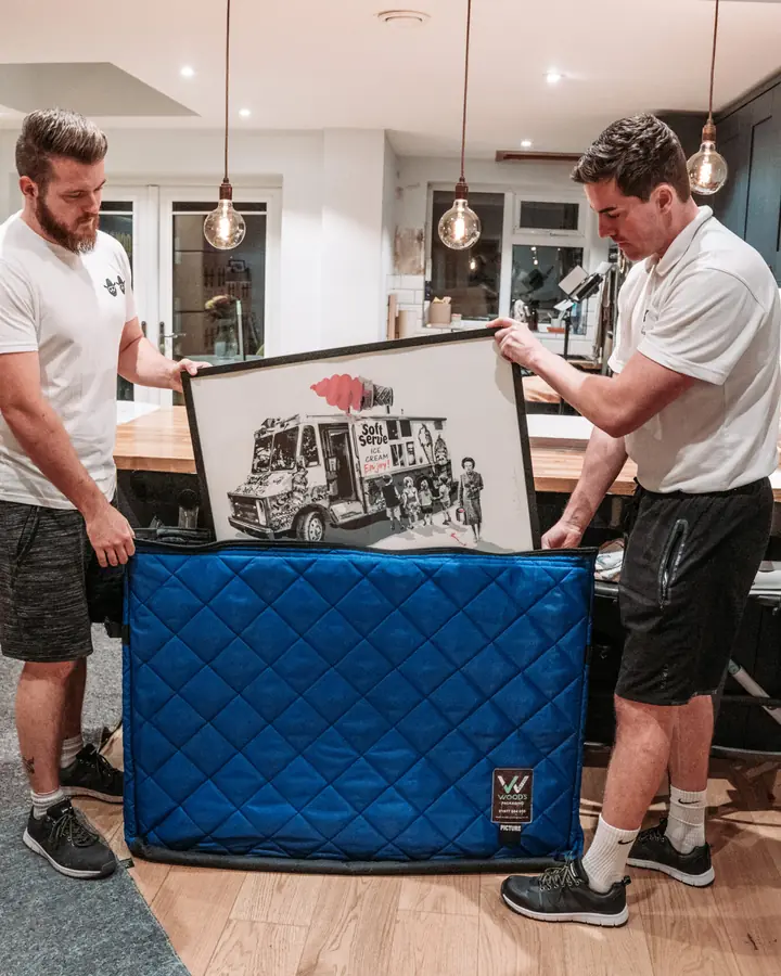 Two Bearded Bros crew members packing a framed picture into a protective picture case in a customer's kitchen