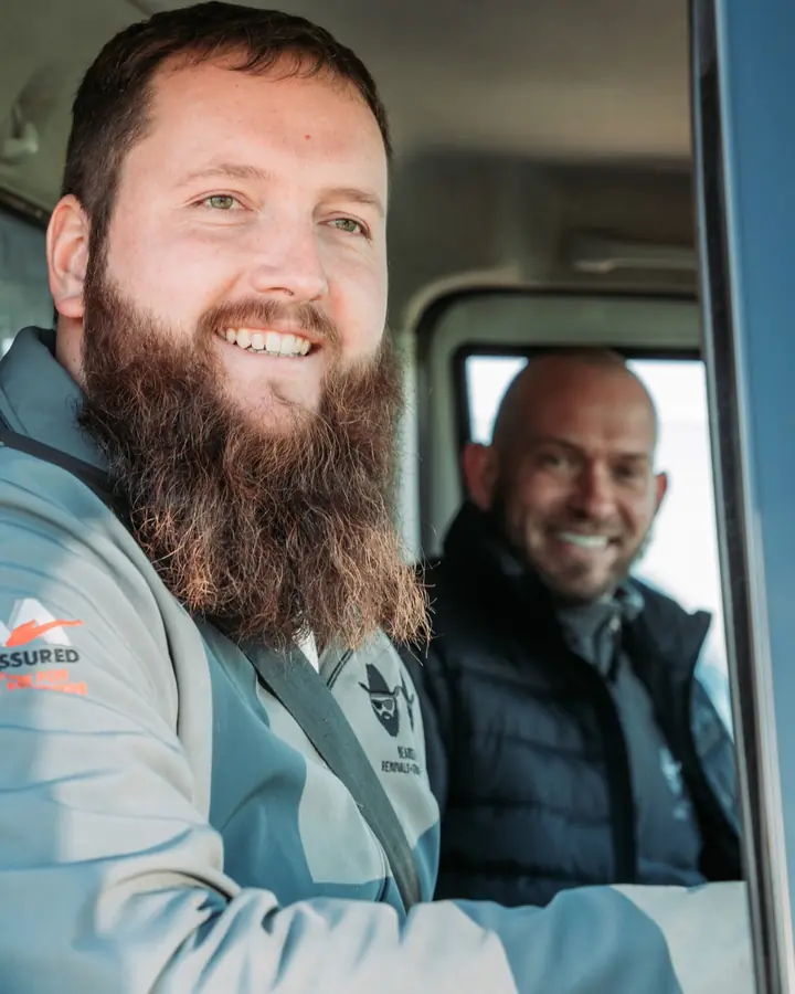 Bearded Bros crew member wearing a Move Assured branded jacket, smiling from inside a removals van cab with a colleague