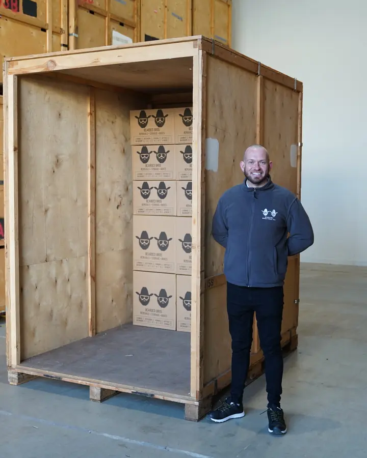 Bearded Bros team member standing beside a wooden storage crate part-filled with branded boxes