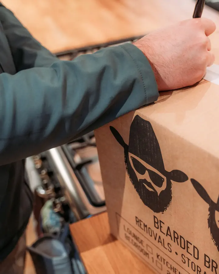 Close-up of a hand labelling a Bearded Bros branded box with tape