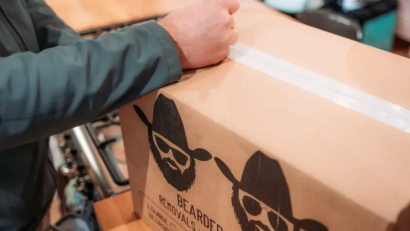 Close-up of a hand labelling a Bearded Bros branded box with tape